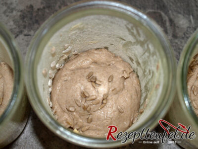 Den Teig in die Gläser geben und mit einigen Sonnenblumenkernen bestreuen